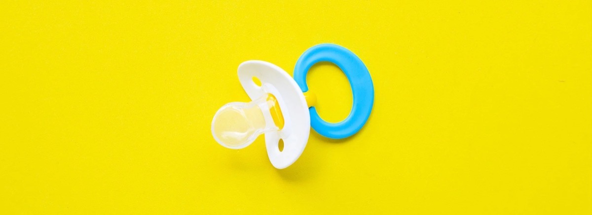 Schnuller mit blauem Ring auf gelbem Hintergrund sinnbildlich für die orthopädische Frühbehandlung in der Kieferorthopädie an den Erlanger Höfen.