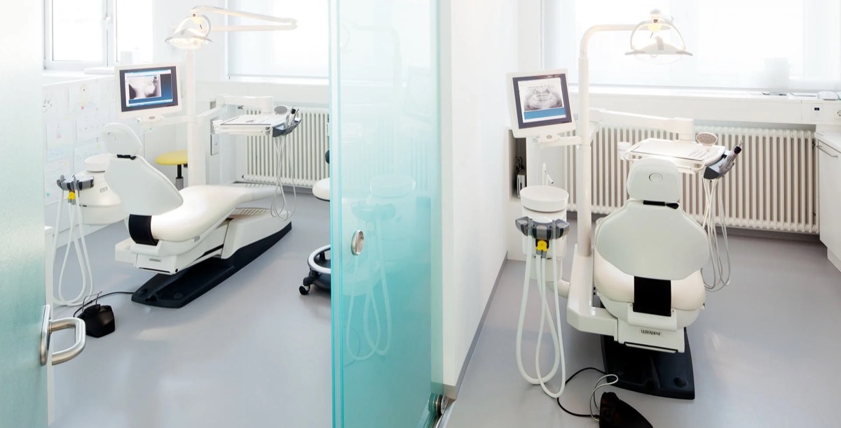Ein Zahnarztzimmer mit Dentalequipment, Stuhl, Bildschirm und bequemer Ausstattung, helles Licht, weiße und neutrale Farben.